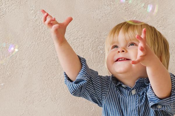 Bild som visar ett litet barn som försöker nå såpubblor inomhus.