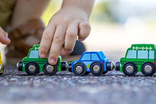 Ett barn sitter på huk utomhus och leker med leksaksbilar i trä.