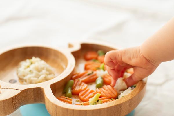 Barnhand griper efter en grönsaksbit från en tallrik.