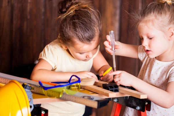 Två flickor i förskoleålder arbetar med verktyg vid en arbetsbänk anpassad för barn.