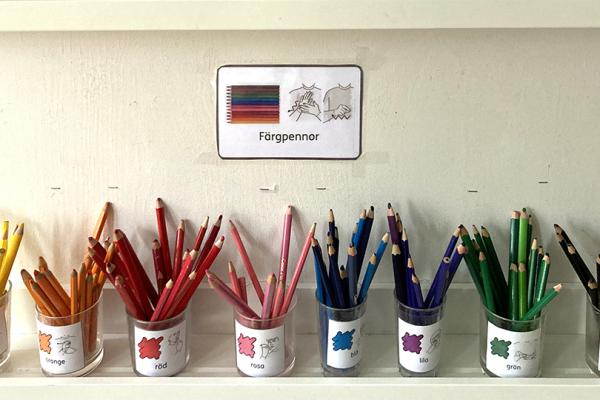 Målarpennor sorterade efter färg i burkar märkta med bildstödskort.