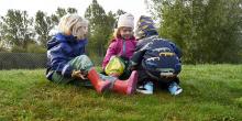 Tre förskolebarn i lek på gräsmatta