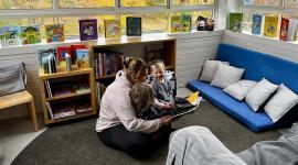 Vuxen läser böcekr för två barn i förskolans läshörna.