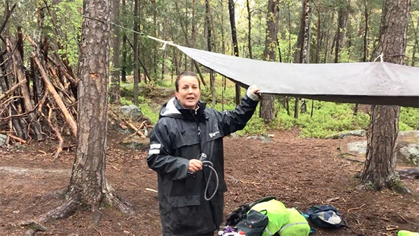 Kvinna håller i presenning som spänts upp mellan några träd i skogen.