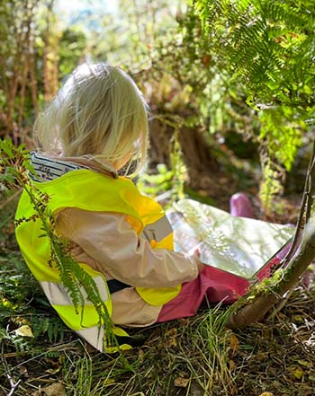 En flicka som sitter och läser en bok i skogen.